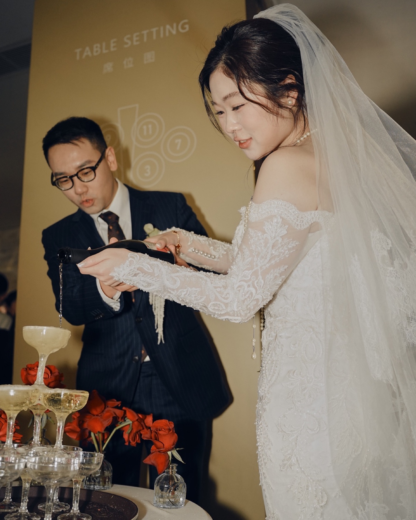 新人共同倒香槟，红色花艺围绕香槟塔